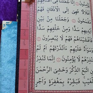 May include: A close-up of a page from a book with Arabic text. The page is bordered in pink and has a pink bookmark with Arabic text. The page number is 75.