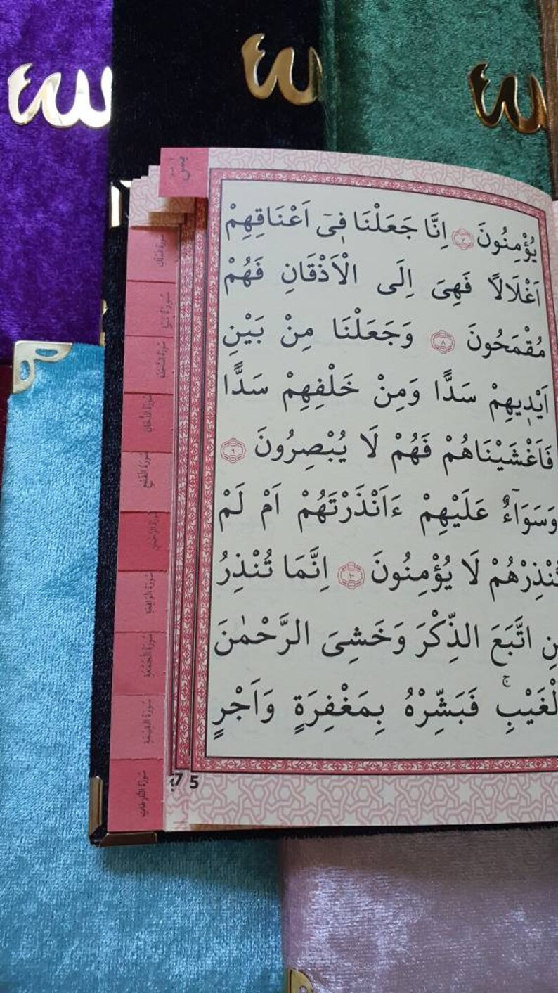 May include: A close-up of a page from a book with Arabic text. The page is bordered in pink and has a pink bookmark with Arabic text. The page number is 75.