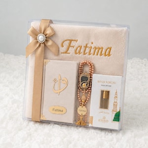 Puede incluir: Un set de regalo en caja transparente que incluye una toalla beige bordada con el nombre Fatima, un libro beige a juego con caligrafía dorada, un rosario de cuentas beige con un dije dorado y un frasco de perfume Ravza Kokusu Misk Aroma.
