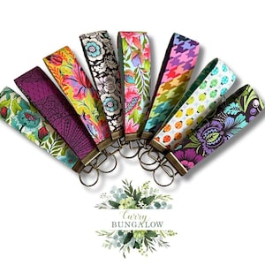 May include: A collection of fabric key fobs in various patterns, including floral, geometric, and houndstooth designs. Each fob features a metal clasp and key ring. The color palette includes vibrant hues of pink, green, blue, and yellow.
