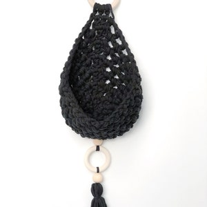 May include: Black macrame hanging planter with a wooden ring and a tassel. The planter is made of cotton cord and has a simple, modern design.