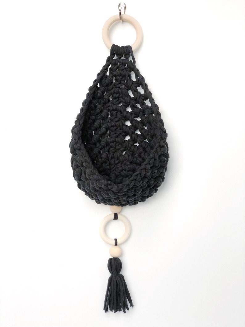 May include: Black macrame hanging planter with a wooden ring and a tassel. The planter is made of cotton cord and has a simple, modern design.