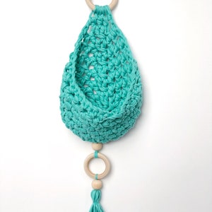 May include: A teal crocheted hanging basket with a wooden ring at the top and a wooden ring with a teal tassel hanging from the bottom.
