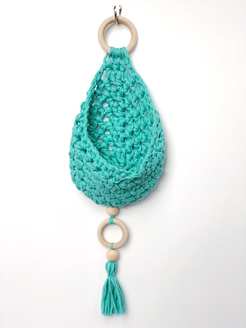 May include: A teal crocheted hanging basket with a wooden ring at the top and a wooden ring with a teal tassel hanging from the bottom.