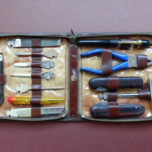 Könnte beinhalten: Ein braunes Lederetui mit Reißverschluss, das verschiedene Werkzeuge enthält, darunter einen schwarzen Stift, eine Zange mit blauen Griffen, zwei Klappmesser, einen kleinen Hammer, einen gelben Schraubendreher, ein Metalllineal und austauschbare Aufsätze.