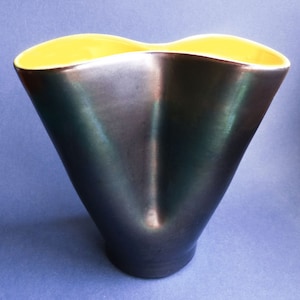 May include: A contemporary vase with a distinctive flared design. The exterior is a dark, metallic grey, contrasting with a bright yellow interior. The vase has a smooth, polished finish, adding to its modern appeal. A decorative home item.