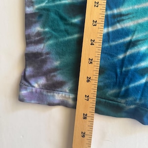 Puede incluir: Un primer plano de una tela de te&ntilde;ido anudado con una regla que mide de 21 a 31 pulgadas. La tela es una mezcla de azul, verde y morado.