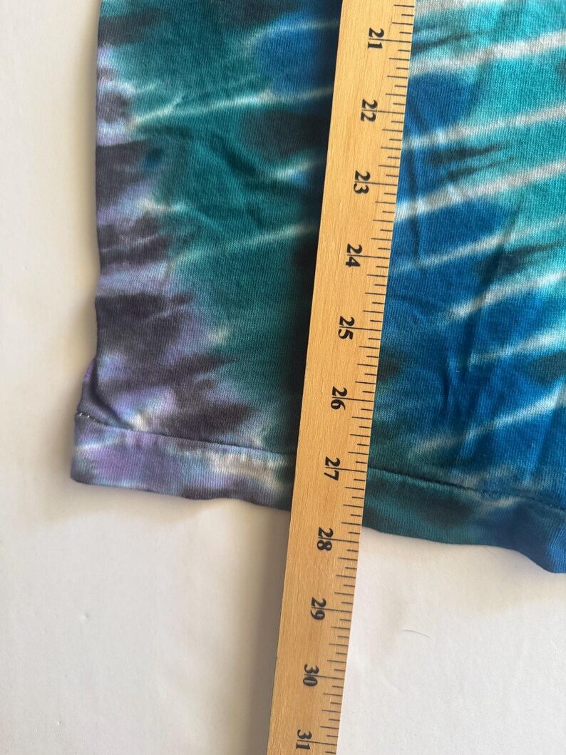 Puede incluir: Un primer plano de una tela de te&ntilde;ido anudado con una regla que mide de 21 a 31 pulgadas. La tela es una mezcla de azul, verde y morado.