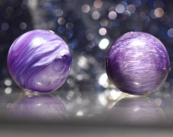 Peut inclure: Deux pierres précieuses sphériques violettes avec un motif blanc tourbillonnant. Les pierres polies reflètent la lumière, créant un effet chatoyant. L'arrière-plan est un ensemble flou de lumières bokeh.
