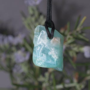 Peut inclure: Un pendentif bleu clair translucide, suspendu &agrave; un cordon noir. La pierre pr&eacute;sente un aspect marbr&eacute; avec des inclusions blanches et brunes. Le pendentif est de forme irr&eacute;guli&egrave;re, sugg&eacute;rant une pierre naturelle.