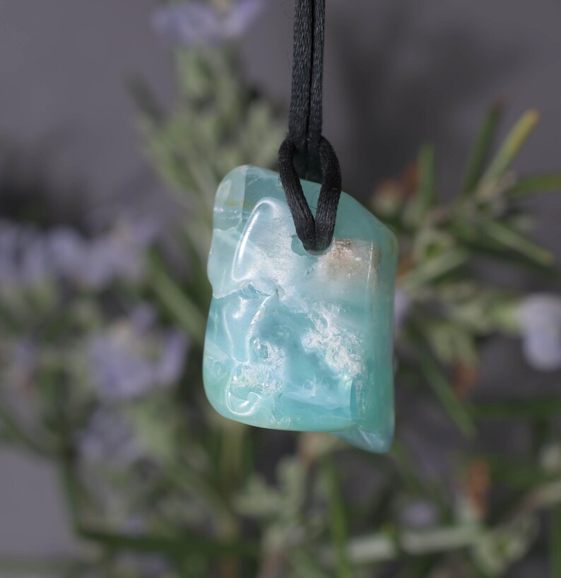 Peut inclure: Un pendentif bleu clair translucide, suspendu &agrave; un cordon noir. La pierre pr&eacute;sente un aspect marbr&eacute; avec des inclusions blanches et brunes. Le pendentif est de forme irr&eacute;guli&egrave;re, sugg&eacute;rant une pierre naturelle.