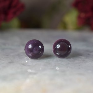 May include: A pair of purple gemstone stud earrings. The earrings are round and have a smooth, polished finish.