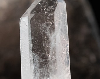 May include: A clear quartz crystal point with a natural, faceted shape. The crystal is about 2 inches tall and has a smooth, polished surface.