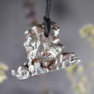 May include: A silver pendant necklace featuring a unique, abstract, and textured design. The pendant is shaped like a jagged rock or mountain.