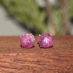 May include: A pair of silver stud earrings with pink ruby gemstones. The earrings are set in a simple, classic style.