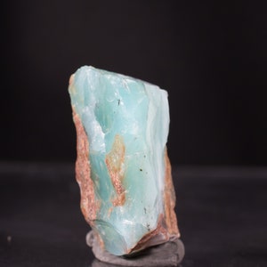 Op de afbeelding: Een groot, ruw gezaagd stuk blauwgroene chalcedoon met bruine insluitsels. De steen is doorschijnend en heeft een glad, gepolijst oppervlak.