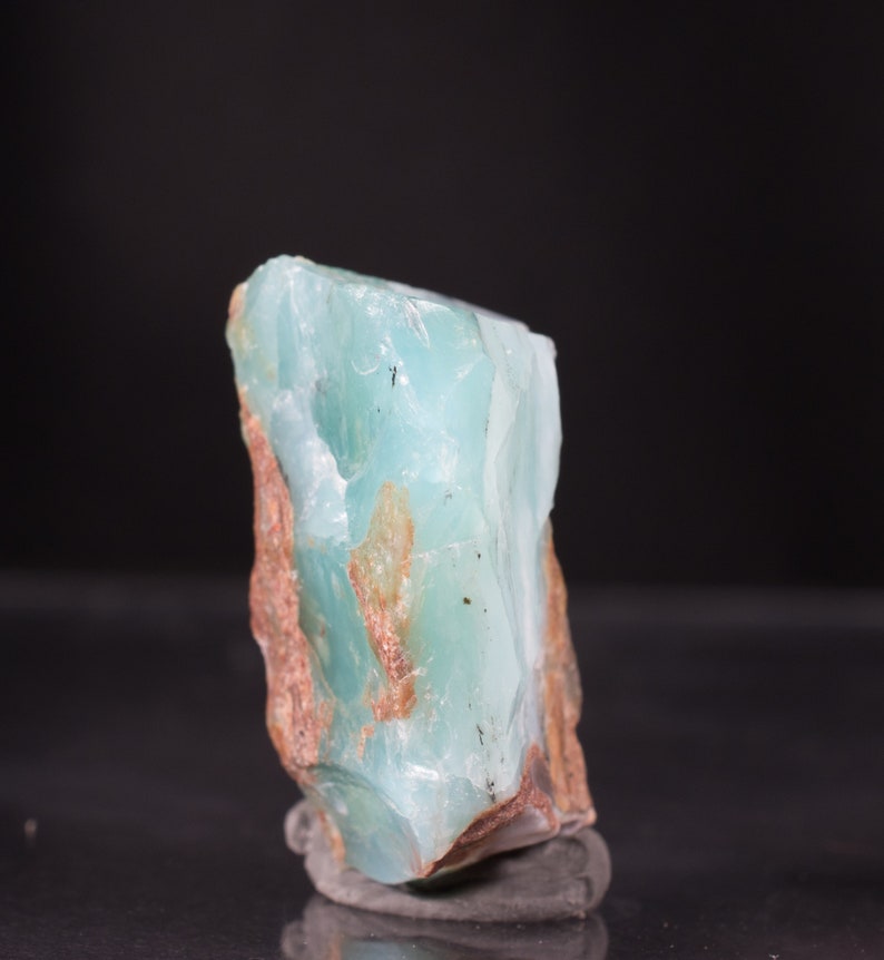 Op de afbeelding: Een groot, ruw gezaagd stuk blauwgroene chalcedoon met bruine insluitsels. De steen is doorschijnend en heeft een glad, gepolijst oppervlak.