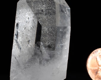 May include: A clear quartz crystal point with a natural, rough base. The crystal is approximately 2 inches tall and is displayed on a black base.