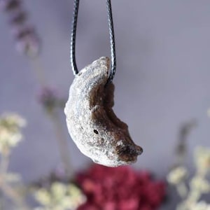Puede incluir: Un colgante en forma de media luna hecho de piedra natural, colgado de un cord&oacute;n negro.