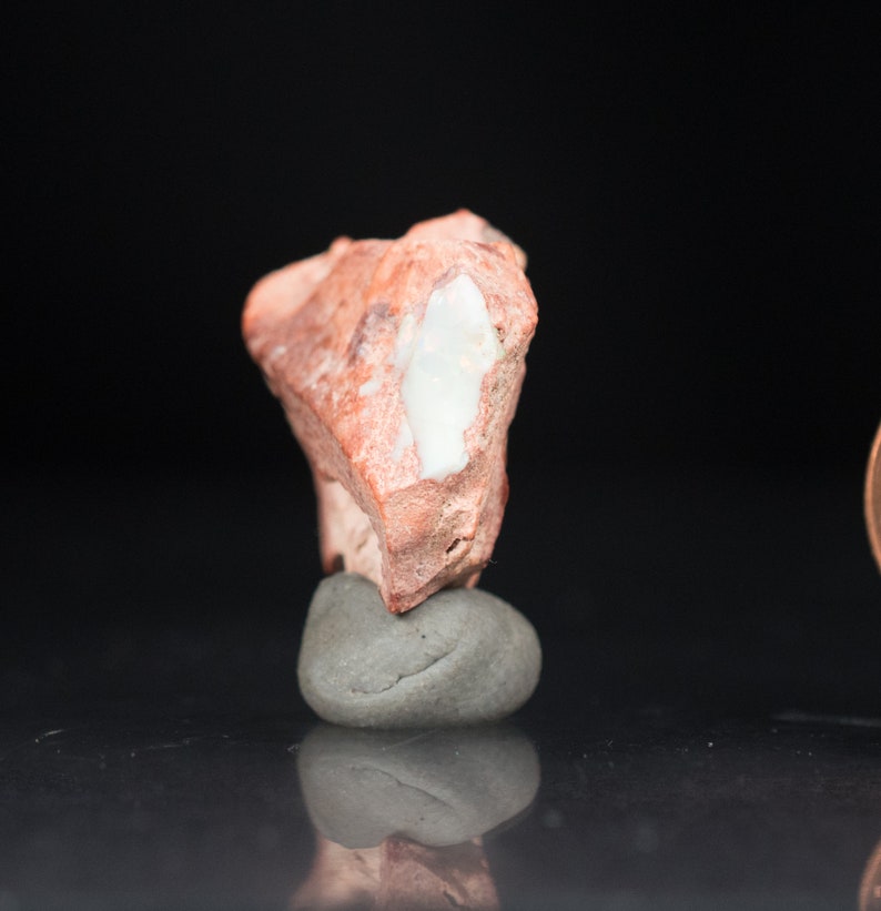 May include: A rough, reddish-brown rock with a white, elongated inclusion, resting on a small, gray stone. The rock's surface has a textured appearance. The background is a solid black.