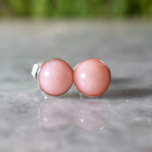May include: A pair of silver stud earrings with pink opal stones.
