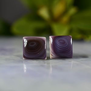 May include: A pair of square-shaped earrings with a purple and white swirl pattern.