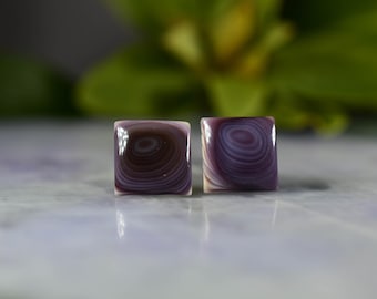 Puede incluir: Un par de pendientes cuadrados con un patrón de espiral morado y blanco.