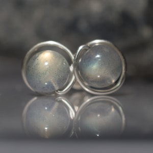 May include: A pair of silver earrings featuring iridescent labradorite gemstones. The gemstones are set in a simple wire frame.