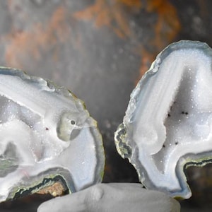 Op de afbeelding: Twee helften van een agaatgeode met een wit, kristallijn interieur en een blauw, groen en bruin gebandeerd exterieur.