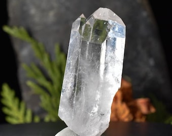 May include: A clear quartz crystal with a double termination. The crystal is about 2 inches long and has a natural, rough texture.
