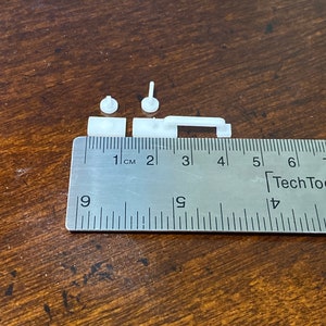 Puede incluir: Piezas de pl&aacute;stico blanco para un modelo impreso en 3D, medidas con una regla con marcas en cent&iacute;metros. Las piezas miden aproximadamente 1 cent&iacute;metro de largo.