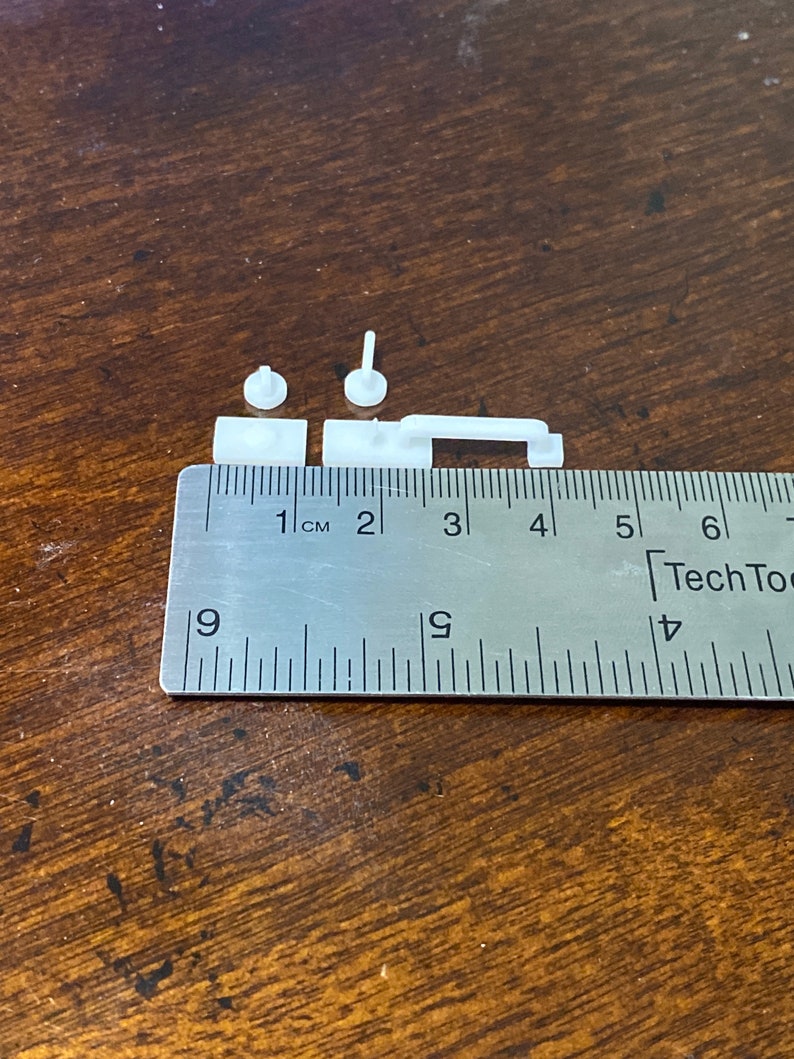 Puede incluir: Piezas de pl&aacute;stico blanco para un modelo impreso en 3D, medidas con una regla con marcas en cent&iacute;metros. Las piezas miden aproximadamente 1 cent&iacute;metro de largo.