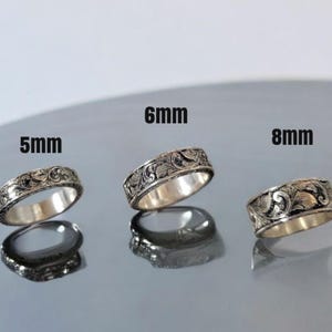 May include: Three silver rings with an intricate floral design. The rings are 5mm, 6mm, and 8mm wide.