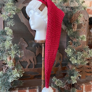 May include: A red and white Santa hat with a long, pointed end and a white pom-pom. The hat features a white knitted band with a brown leather accent. The hat is displayed on a mannequin head.