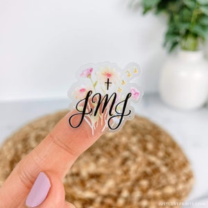 clear JMJ sticker with black letter with flowers in background on a finger
