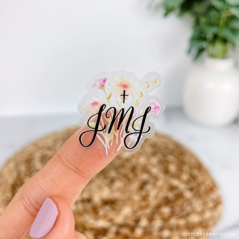 clear JMJ sticker with black letter with flowers in background on a finger