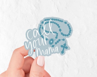 May include: A light blue sticker featuring a dark blue rosary illustration and the white cursive text call your mama. The sticker has a die-cut shape that follows the outline of the rosary beads and the cross, creating a cohesive graphic design.