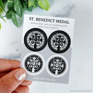 May include: A sheet of four mini vinyl stickers featuring the St. Benedict Medal design. Two stickers are black with white details, and two are white with black details. The text reads ST. BENEDICT MEDAL, dishwasher safe & weatherproof, and JustLovePrints.com.