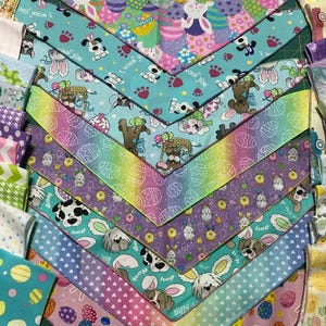 May include: A collection of colorful fabric bandanas with Easter-themed designs, including bunnies, eggs, and flowers. The bandanas are arranged in a fan shape, with the top bandana featuring the text "I woof you".