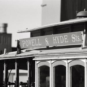 May include: Black and white photograph of a vintage cable car with the sign "Powell & Hyde Sts." above the windows.