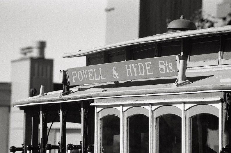 May include: Black and white photograph of a vintage cable car with the sign "Powell & Hyde Sts." above the windows.