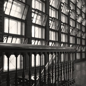 K&ouml;nnte beinhalten: Ein schwarzes Metallgel&auml;nder mit dekorativen Spindeln, das zu einer Treppe f&uuml;hrt. Das Gel&auml;nder befindet sich vor einem gro&szlig;en Fenster mit vielen Fensterscheiben, die ein geometrisches Muster bilden.