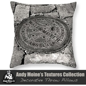 Può includere: Fotografia in bianco e nero di un coperchio di contatore dell'acqua vintage con il testo "SEWERAGE & WATER BOARD CRESCENT BOX WATER METER NEW ORLEANS, LA." Il coperchio è posto su uno sfondo di ciottoli.