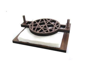 May include: A dark brown wooden napkin holder with a geometric design. The holder has a round base and two vertical posts.