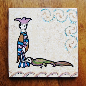 May include: A hand-painted ceramic tile with a whimsical design featuring a bird with a pink hat and a green lizard. The tile has a white background with blue and gold swirls.