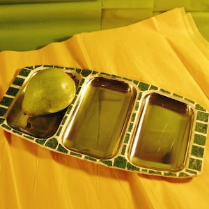 May include: A green and white ceramic serving tray with three compartments. The tray has a pear-shaped fruit in one compartment.