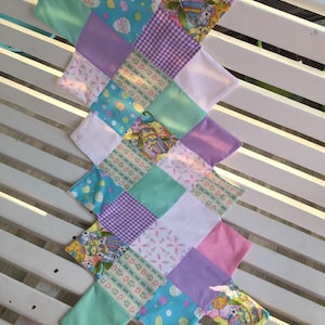 May include: A patchwork quilt with a variety of Easter-themed fabrics, including pastel colors, eggs, and bunnies. The quilt is made up of squares and rectangles, and is sewn together with a white thread.