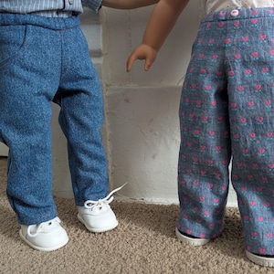 Puede incluir: Dos pantalones para muñeca. Un par es de color azul sólido con tela texturizada, con cintura y bolsillos laterales. El segundo par es azul claro con un patrón repetitivo de pequeñas flores rosas y tallos verdes, con cintura y un botón de color rosa.