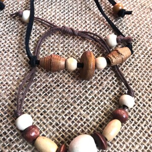 Puede incluir: Dos collares de cordón de cuero marrón con cuentas de madera en varios tonos de marrón, beige y blanco. Las cuentas son redondas, ovaladas y cilíndricas.