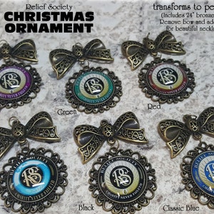 May include: Six different colored Christmas ornaments with a gold filigree design. Each ornament features a gold 'RS' logo with the words 'Relief Society' and 'Charity Never Faileth' around the logo. The ornaments are available in purple, green, red, blue, black, and global.